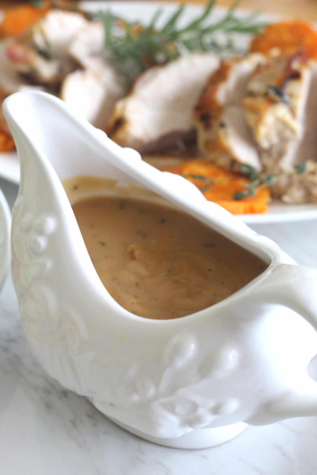 White wine gravy with herbs served in a gravy bowl. In the background you see a platter with sliced roasted turkey and herbs!