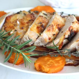 A platter with roasted turkey breast, sweet potatoes and fresh herbs.
