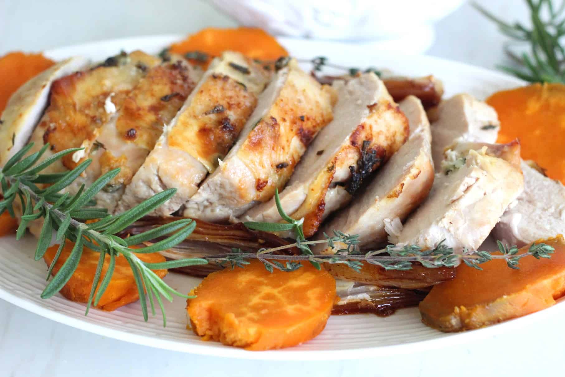 Roasted turkey breast on a platter, accompanied with herbs, sweet potato slices.
