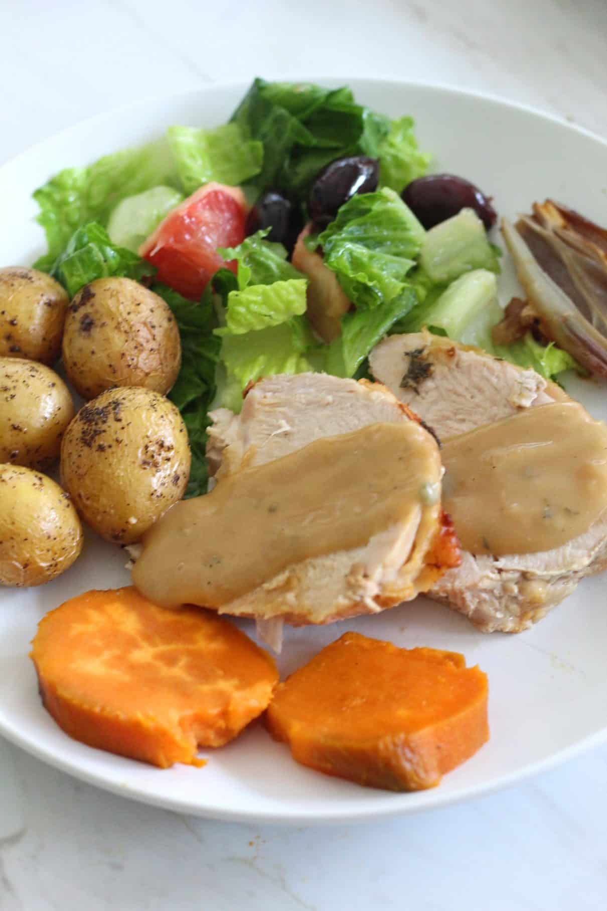 Served plate with roasted potatoes, roasted turkey breast slices, vegetables. Turkey breast slices are covered in gravy.