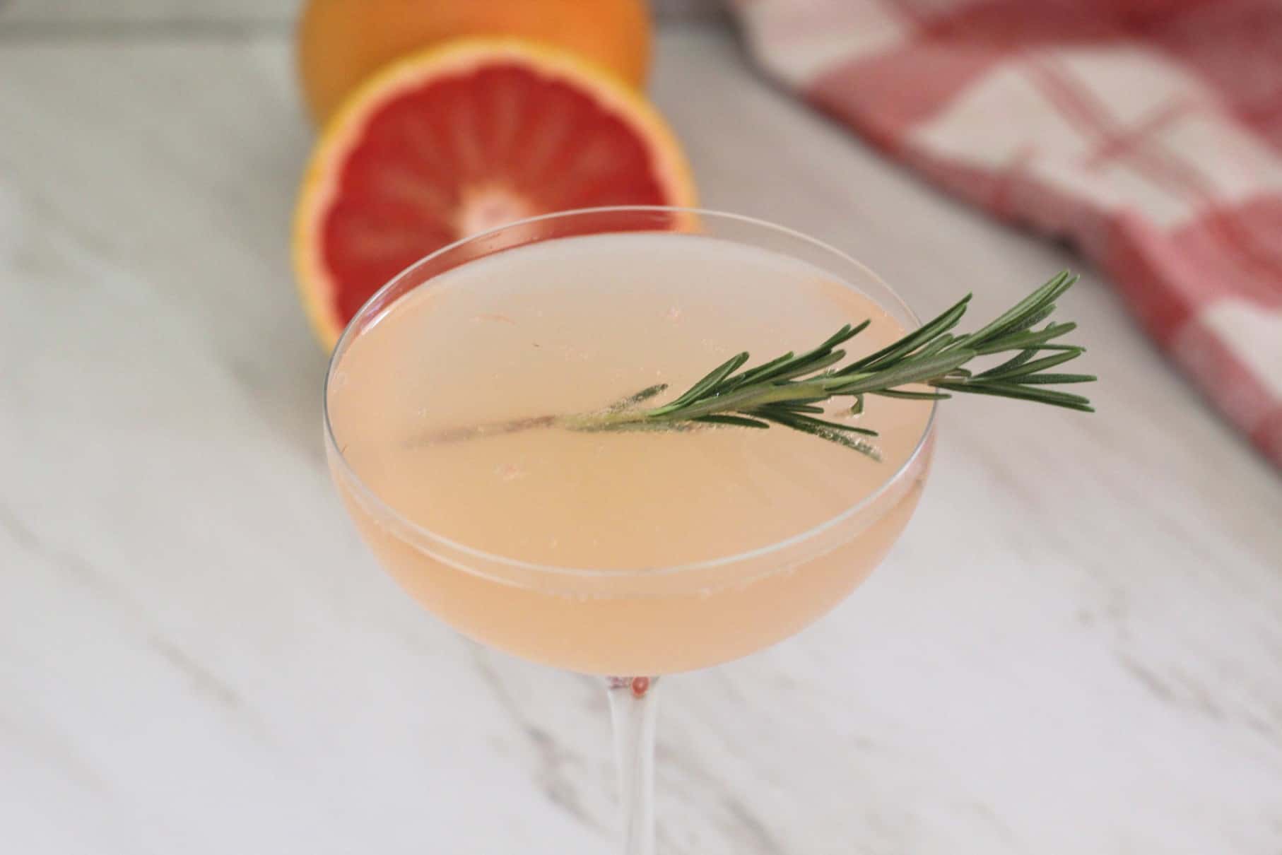 A coupe glass with a pink cocktail made with elderflower syrup, prosecco and grapefruit. 