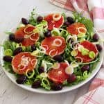 A salad platter with greens, blood orange, olives and leeks.