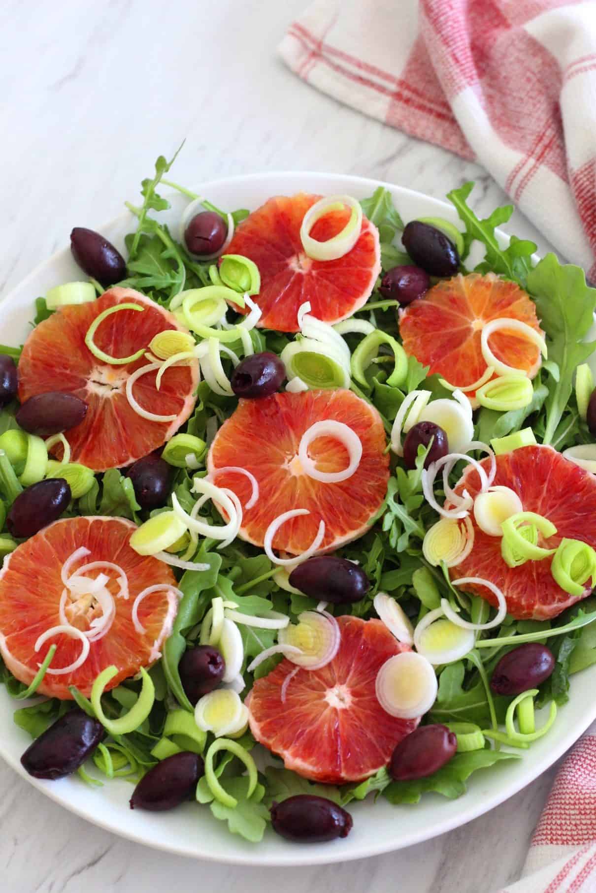 A platter of blood orange salad and leeks. You can see arugula leaves and kalamata olives too. 