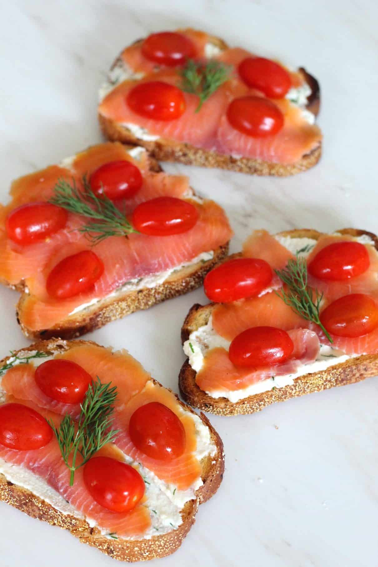 Ricotta crostini topped with smoked salmon, cherry tomatoes, dill and olive oil. This picture shows 4 crostini at different angles