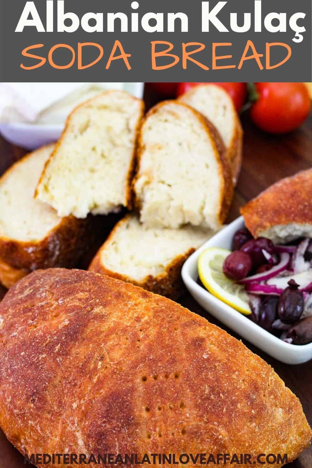 Homemade soda bread (Kulaç) shown cut in half, half is sliced and half is whole. Bread is next to mezes like olives and cheese.