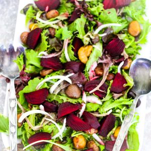 A rectangular salad dish with greens, beets, and chestnuts