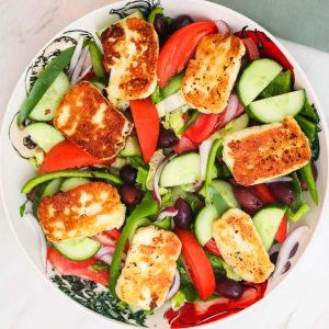A round big salad platter with lots of veggies and fried halloumi cheese