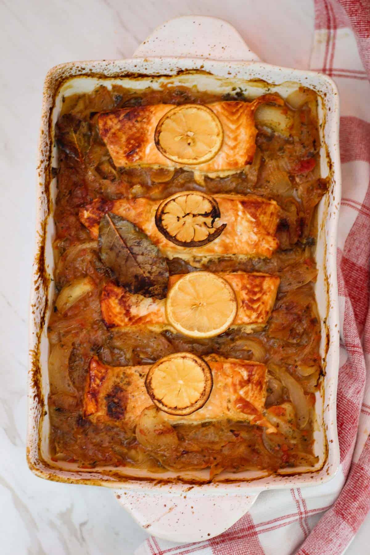 A rectangle baking dish with salmon, onions and lemon. Dish is already baked.