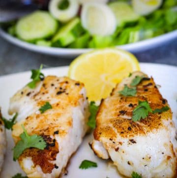 Seared Chilean sea bass on a platter, garnished with cilantro and lemon slices. In the background you see a salad platter.