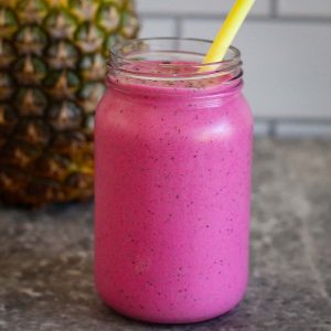 A pineapple, dragon fruit smoothie shown in center and a fresh pineapple is shown in the background.
