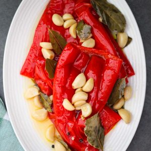 An oval platter with red peppers, garlic, bay leaves, peppercorn etc