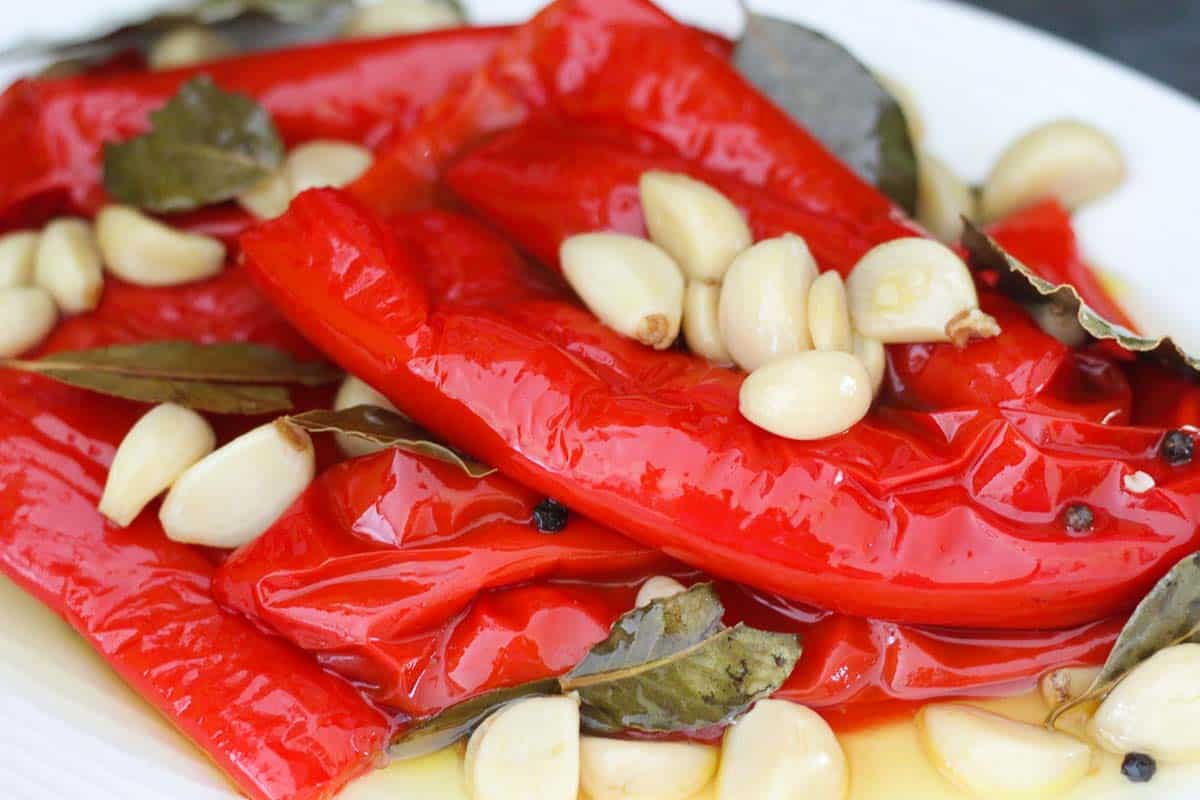Red peppers on a platter, shown with other ingredients they were cooked in. Garlic, bay leaves, pepper corn. 