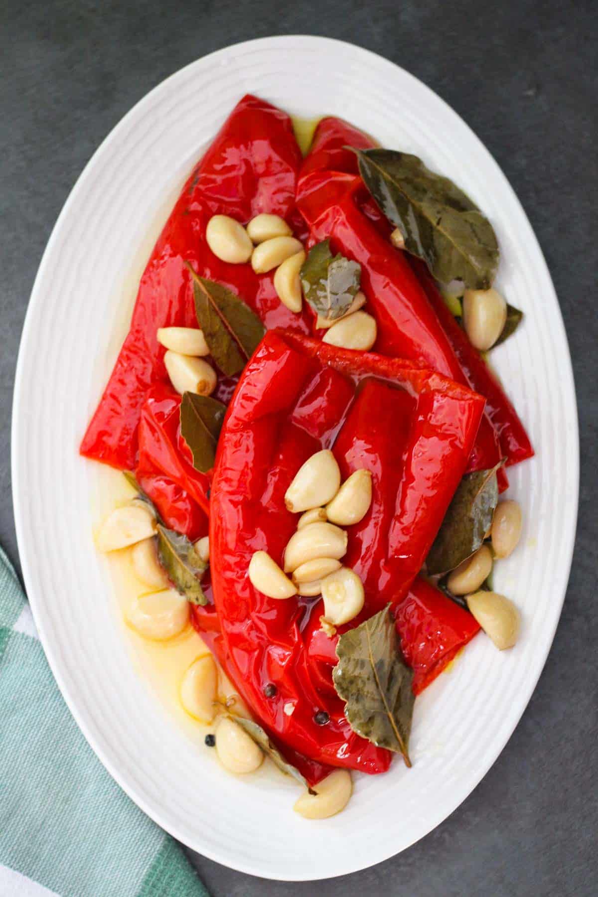 Albanian red peppers cooked in pressure cooker, they're called gogozhare. The peppers are shown served on a platter with garlic, pepper, and bay leaves. 