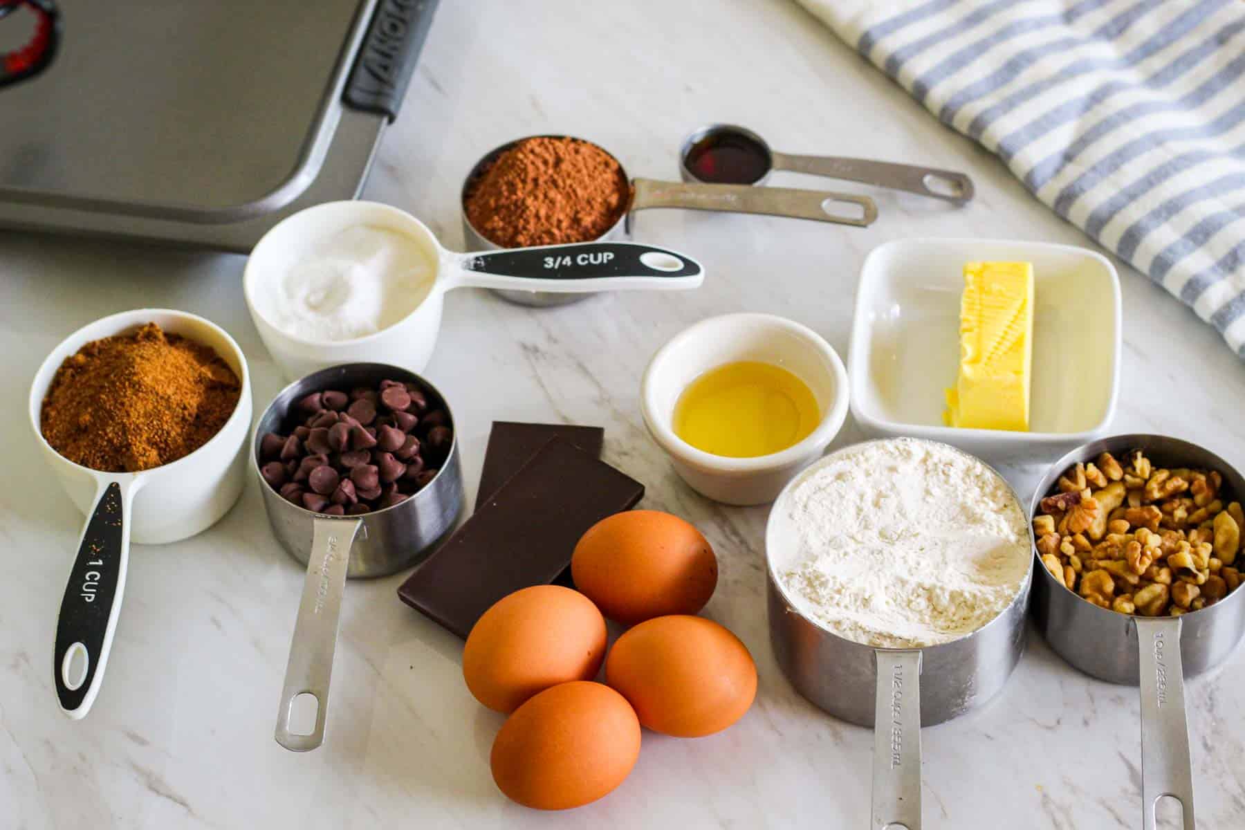 Ingredients for making triple chocolate brownies with walnuts: sugar, brown coconut sugar, cocoa, vanilla, avocado oil, butter, chocolate chips, chocolate bars, eggs, AP flour, chopped walnuts.