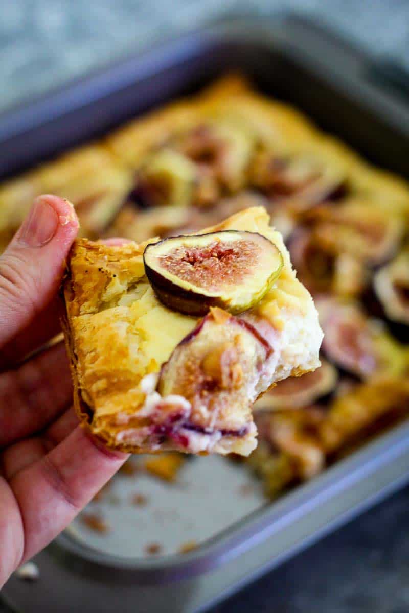 A slice of figs tart lifted up towards the camera while the rest of the tart is in the baking pan on the table.