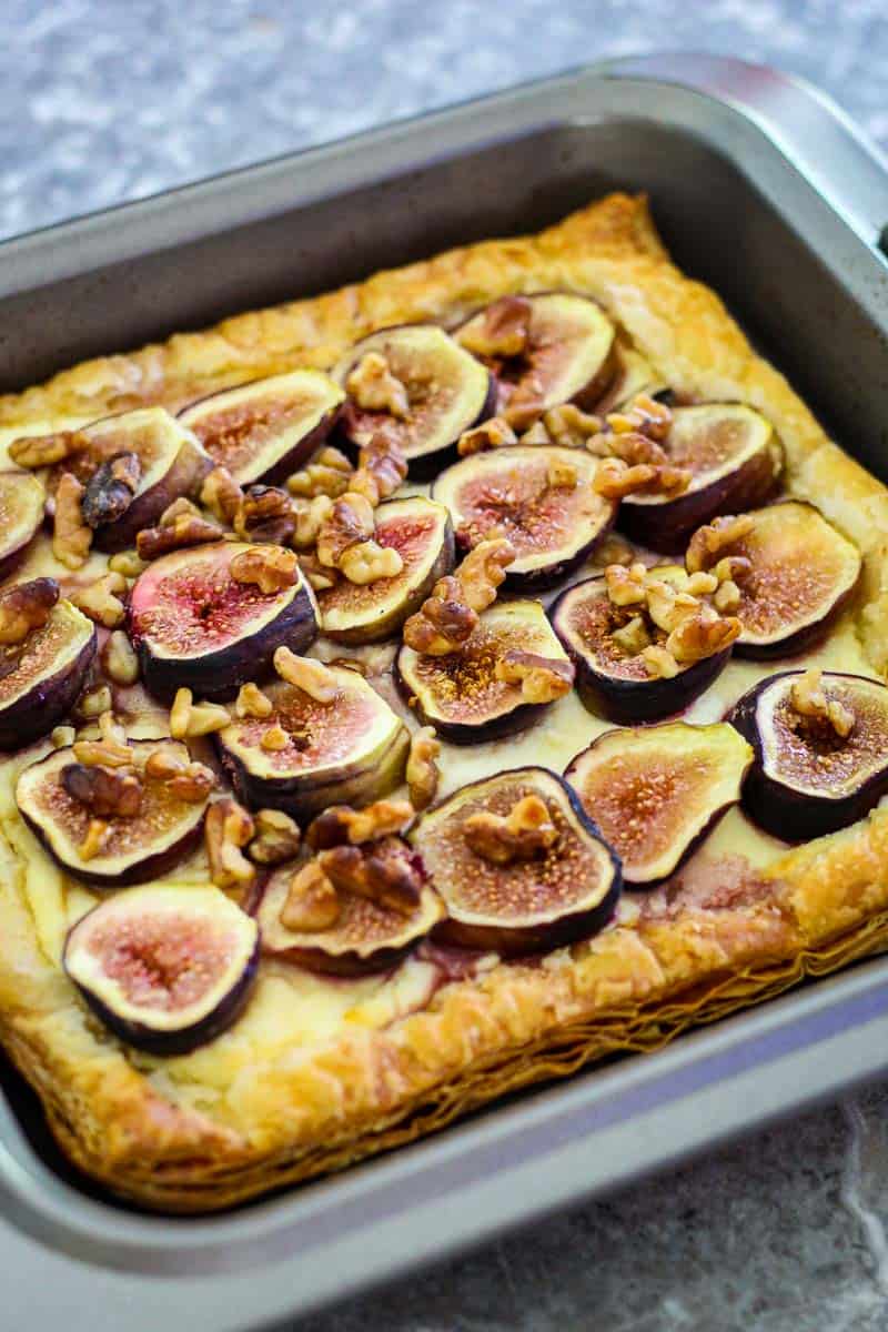 A square baking tray with a baked pastry tart that has figs and walnuts toppings. 