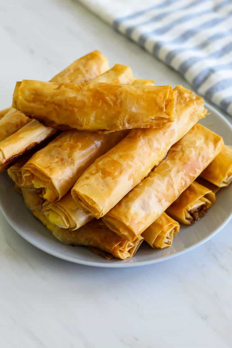 A plate with baked phyllo sticks. They look golden brown.