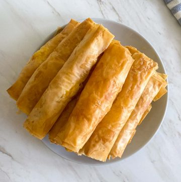 A pile of baked phyllo cheese sticks on a plate, view is from above.