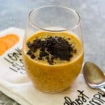A clear glass with pumpkin oatmeal, topped with shaved dark chocolate