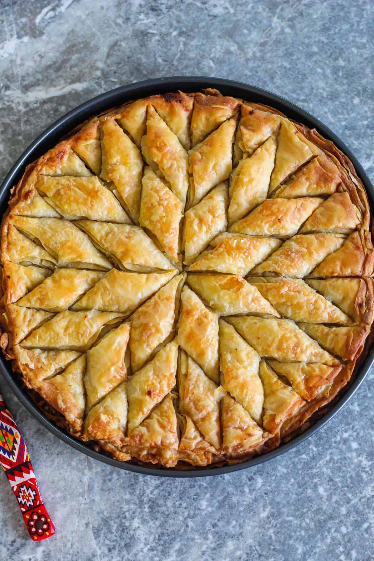 Homemade baklava from scratch, already baked and cut in the traditional rhombus shape. Baklava is shown on a round baking tray.