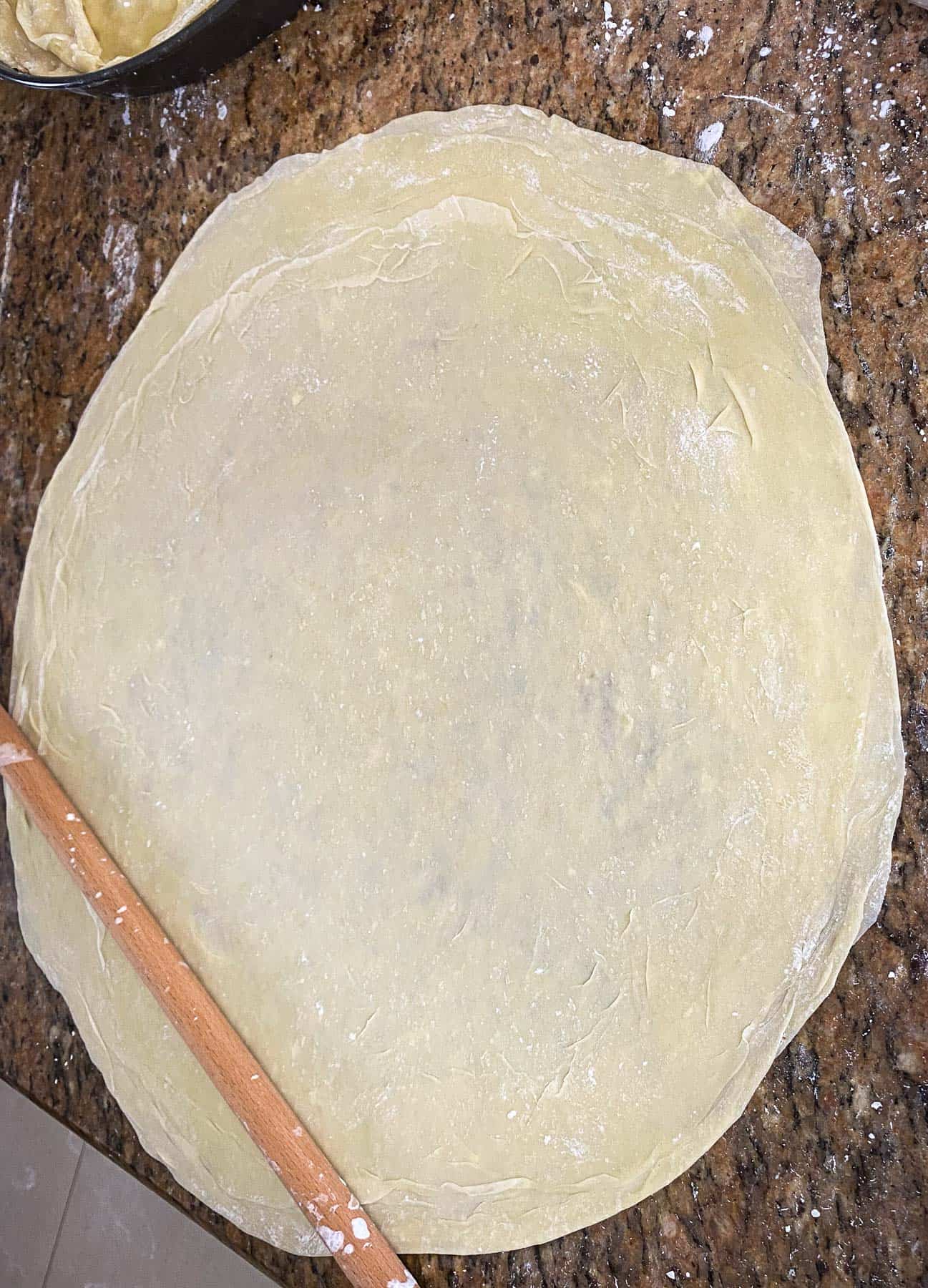 One layer of phyllo shown on a flat surface being rolled with Albanian rolling pin called Okllai.