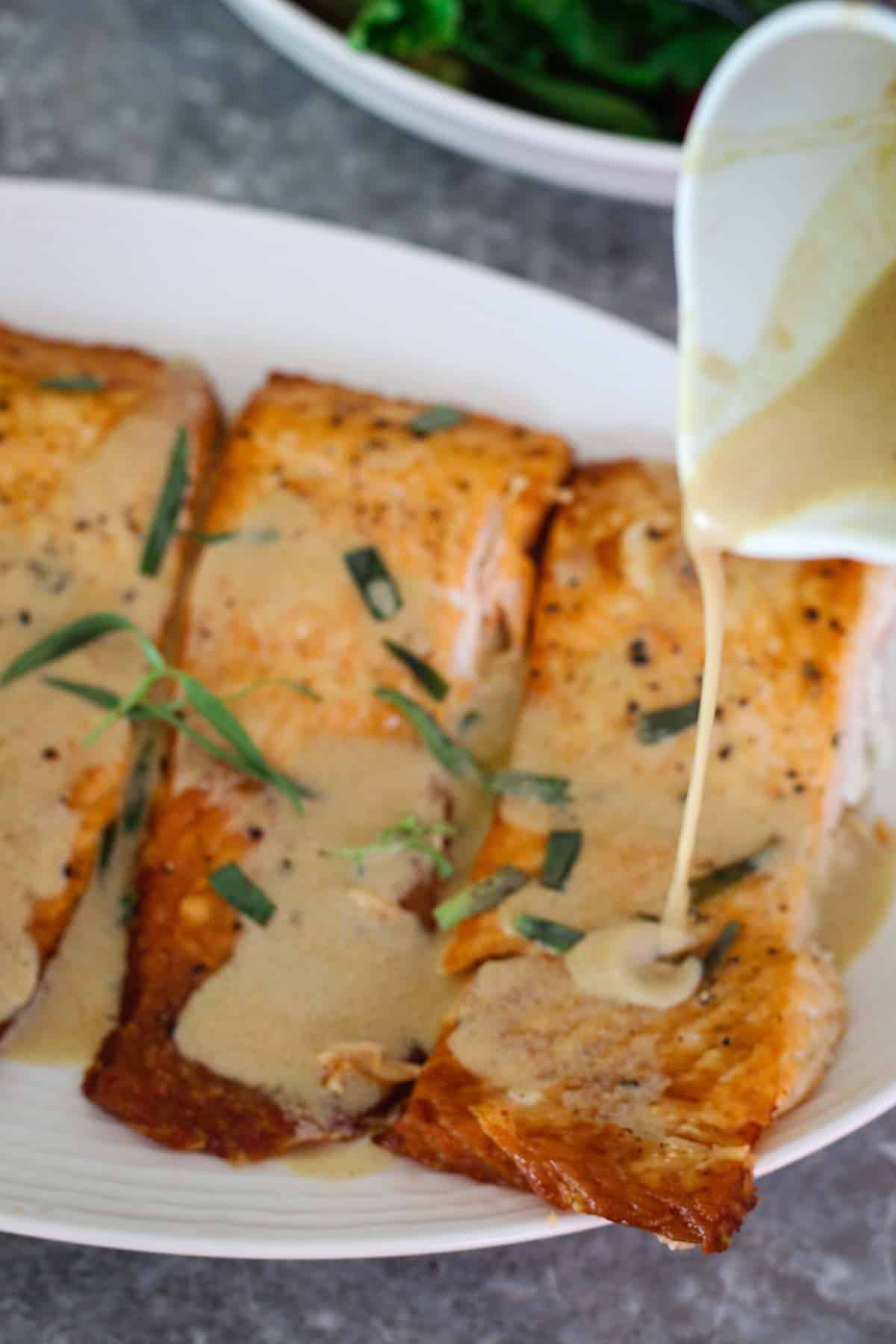 Pouring Dijon, Tarragon Sauce over salmon, Picture shows a cup pouring the sauce over cooked salmon.