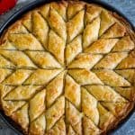 A round baking dish with baklava in it, baklava is baked and cut in diamond shapes that radiate from center out.