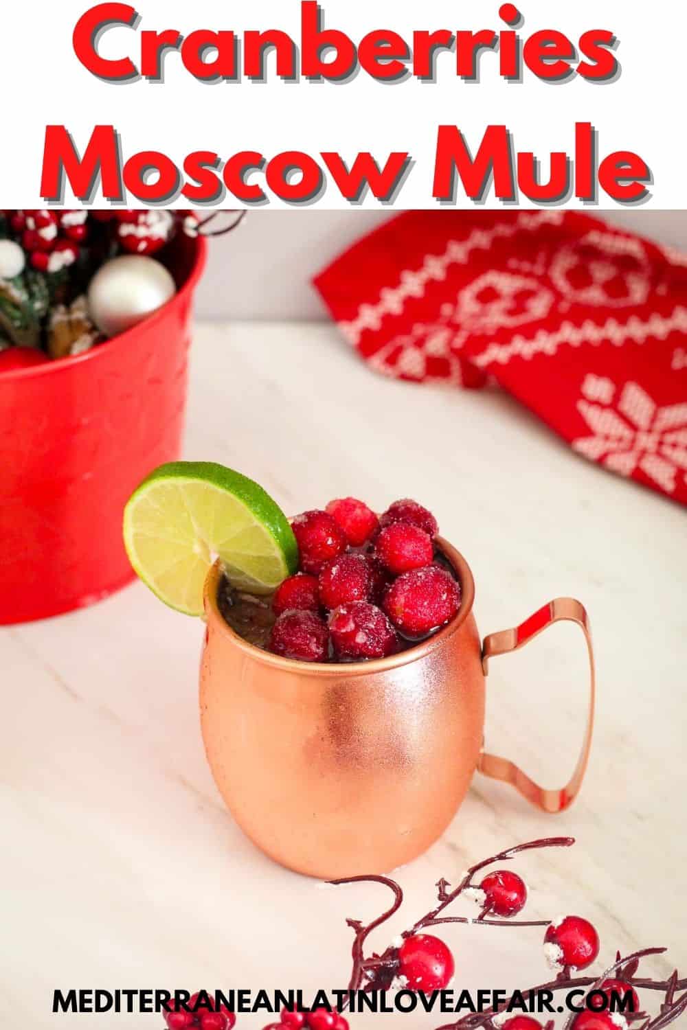 An image of a moscow mule cocktail prepared specifically for Pinterest. Image shows a sugared cranberries cocktail on a copper mug, garnished with lime slice. There's a title bar on top and the website link on the bottom.