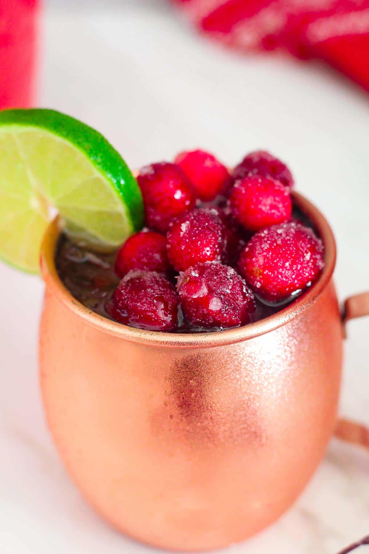 A copper mug with a drink in it, topped with frozen sugared cranberries and a lime slice. 