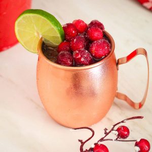 A copper mug with a col cocktail, shown topped off with frozen sugared cranberries and garnished with a lime slice.