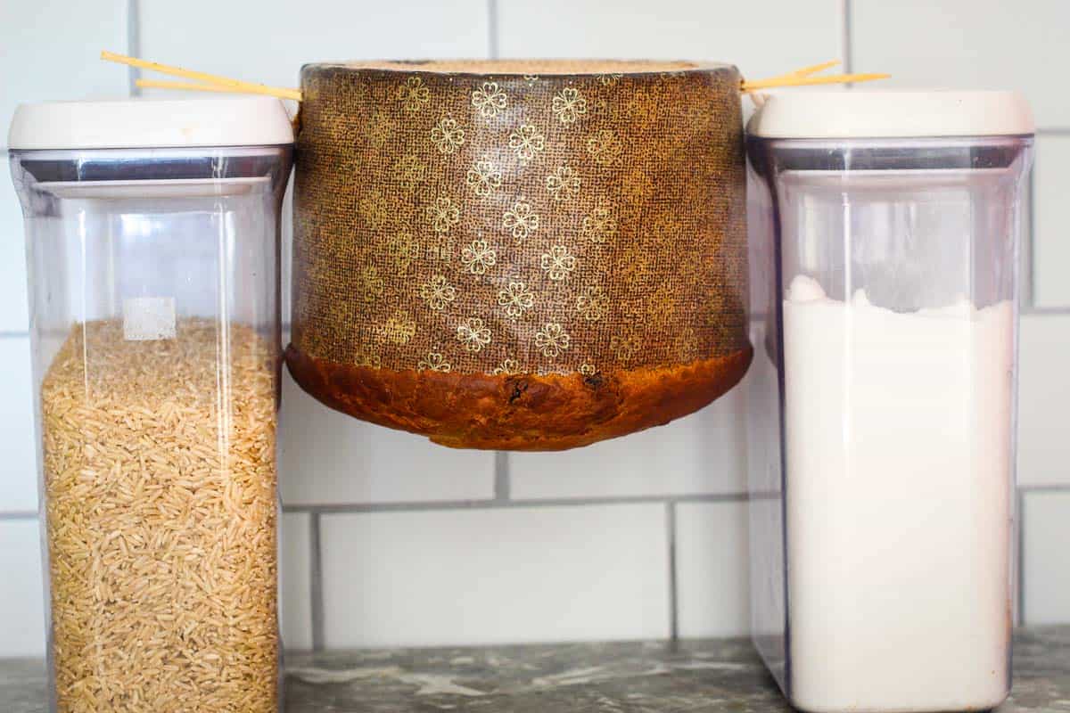 Picture shows a panettone in skewers, hanging upside down next to two kitchen containers.