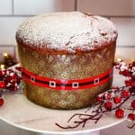 Raisins and candied fruits panettone on a cake holder, garnished with confectioner sugar .