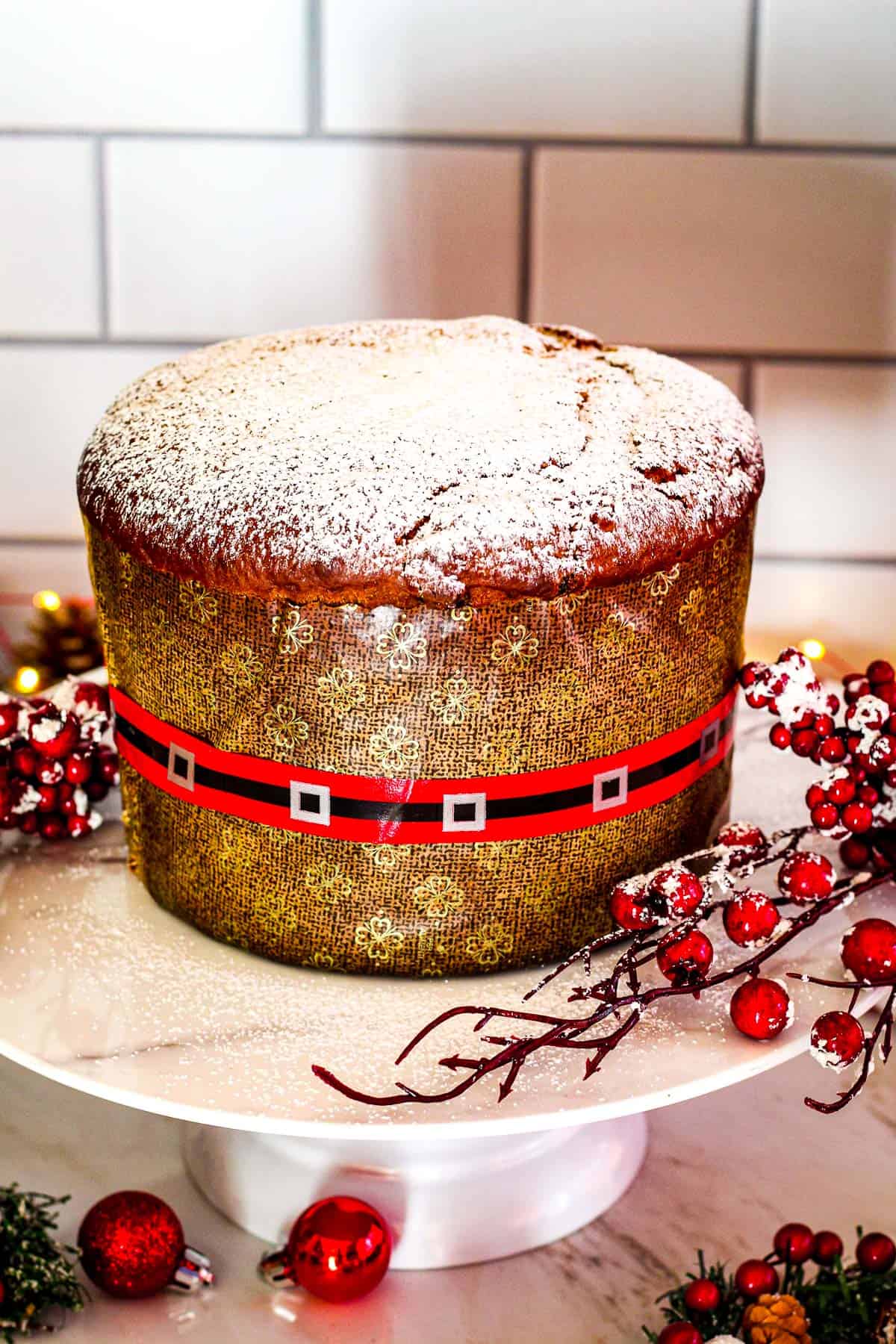 A panettone on a cake holder, dusted with confectioner sugar and lots of festive decorations. 