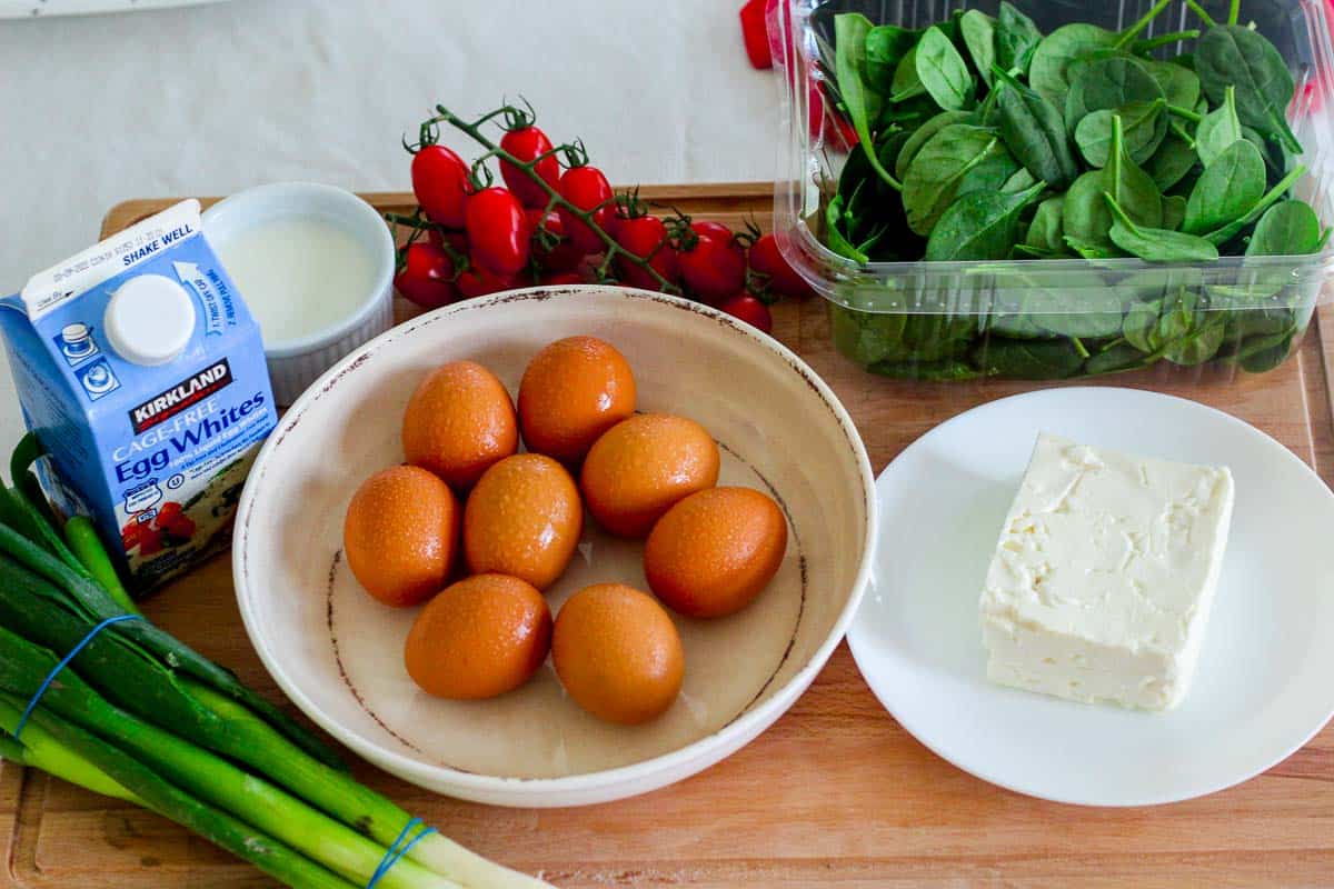 Raw ingredients for frittata before cooking. Eggs, egg whites, feta cheese, spinach, cherry tomatoes, milk, green onions.