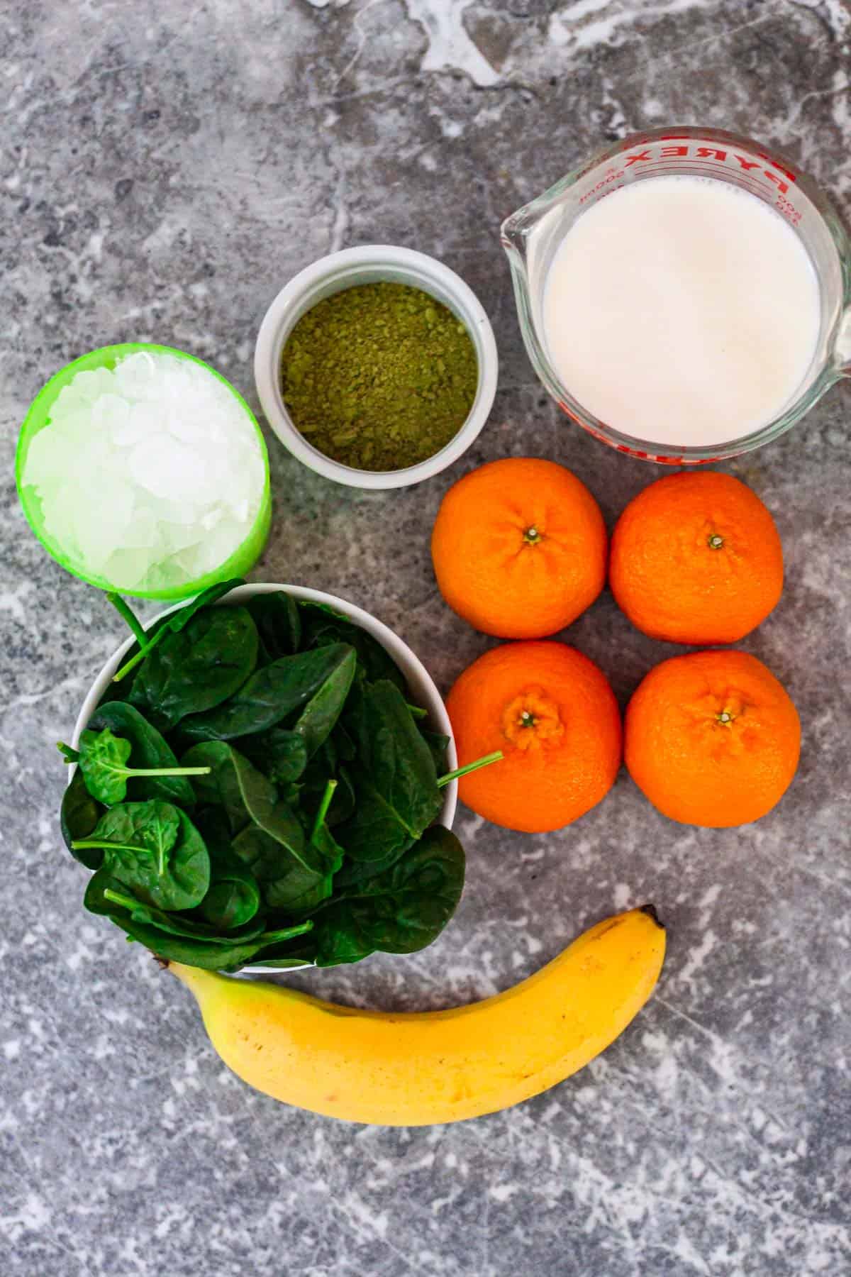Ingredients for two smoothies: ice, matcha powder, milk, spinach, mandarins and banana.
