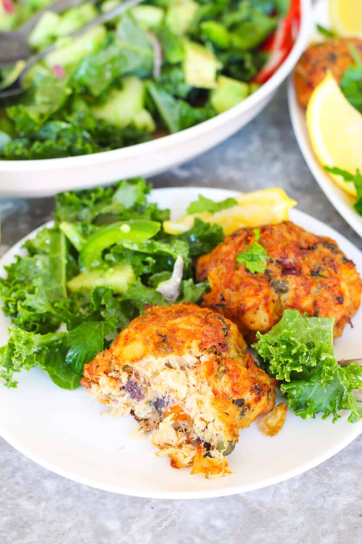 A serving of Cod Fish cakes with salad. On of the cod cakes is bitten and you can see inside the fish cake. 