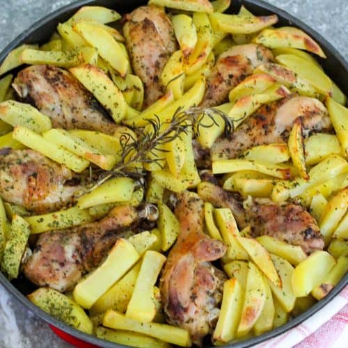 A casserole with baked chicken drumsticks and potatoes arranged in a circular shape.