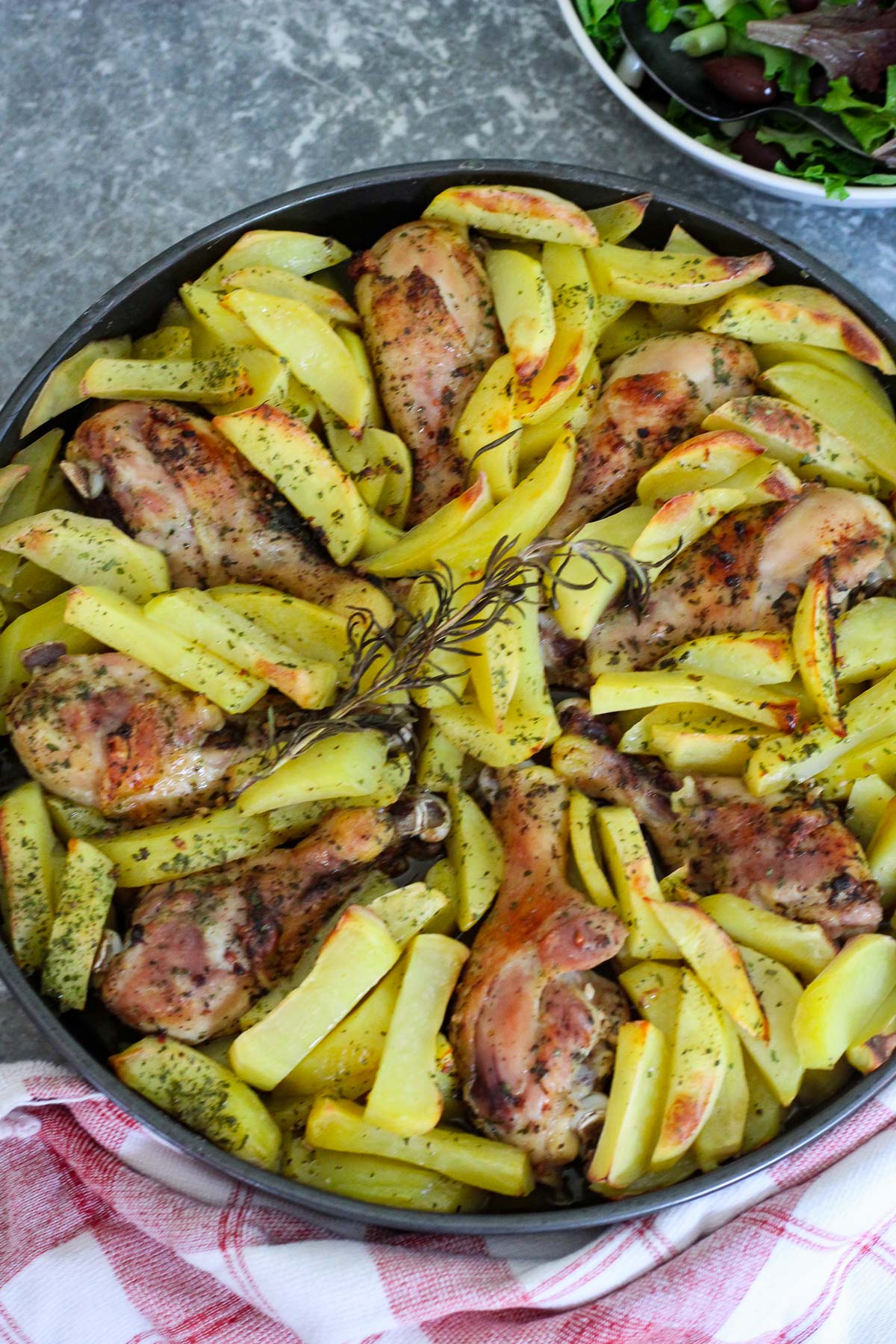 A round deep baking dish shown with baked potatoes and chicken drumsticks. Drumsticks are arranged in a circular pattern.