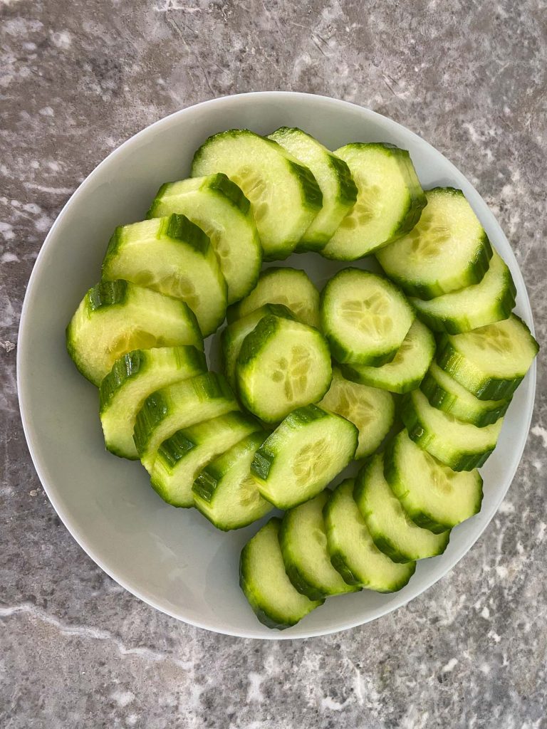 Striped cucumber, then sliced. All slices are placed on a plate in a round pattern.