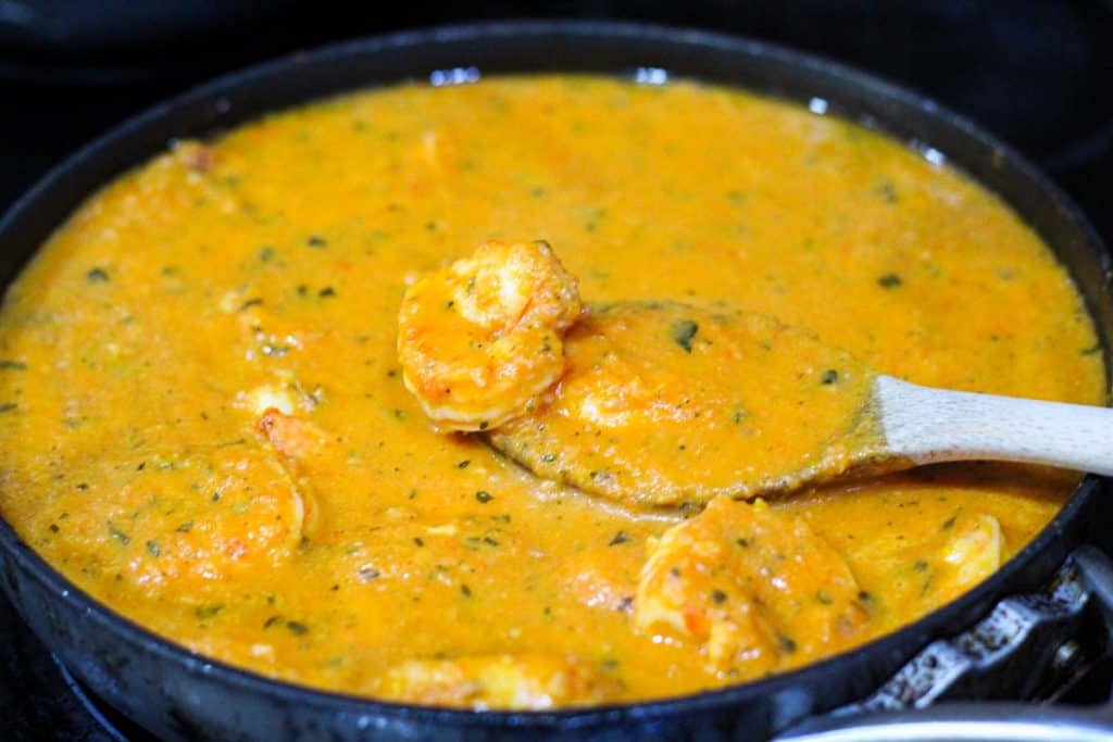 Roasted tomato sauce is poured over the skillet where shrimp cooked with garlic. 