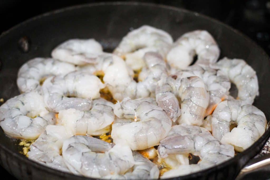 Shrimp is added to skillet to cook with garlic. You can see the edges of the shrimp turning pink as it cooks. 
