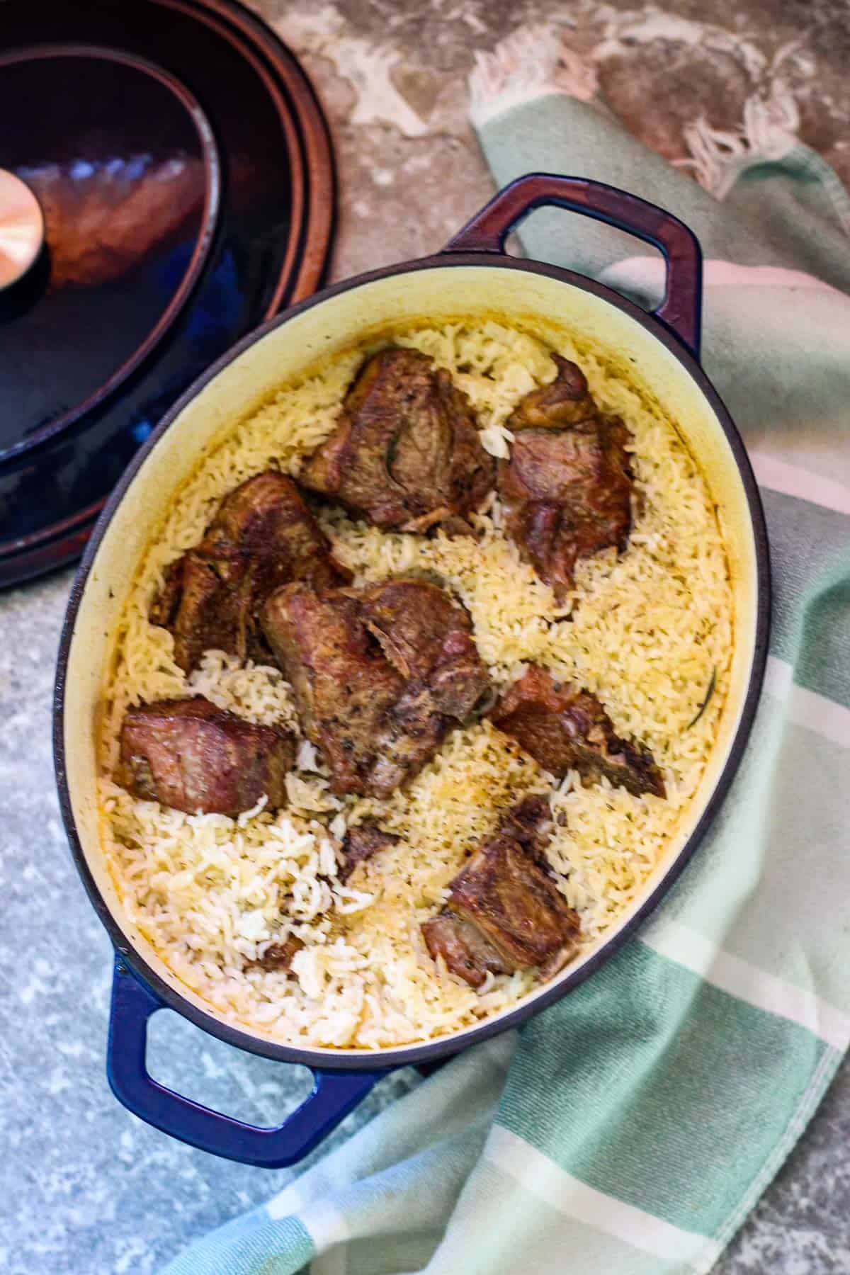 Baked lamb and rice on a Dutch oven, lid is on the side and a towel on the other side of the dish.