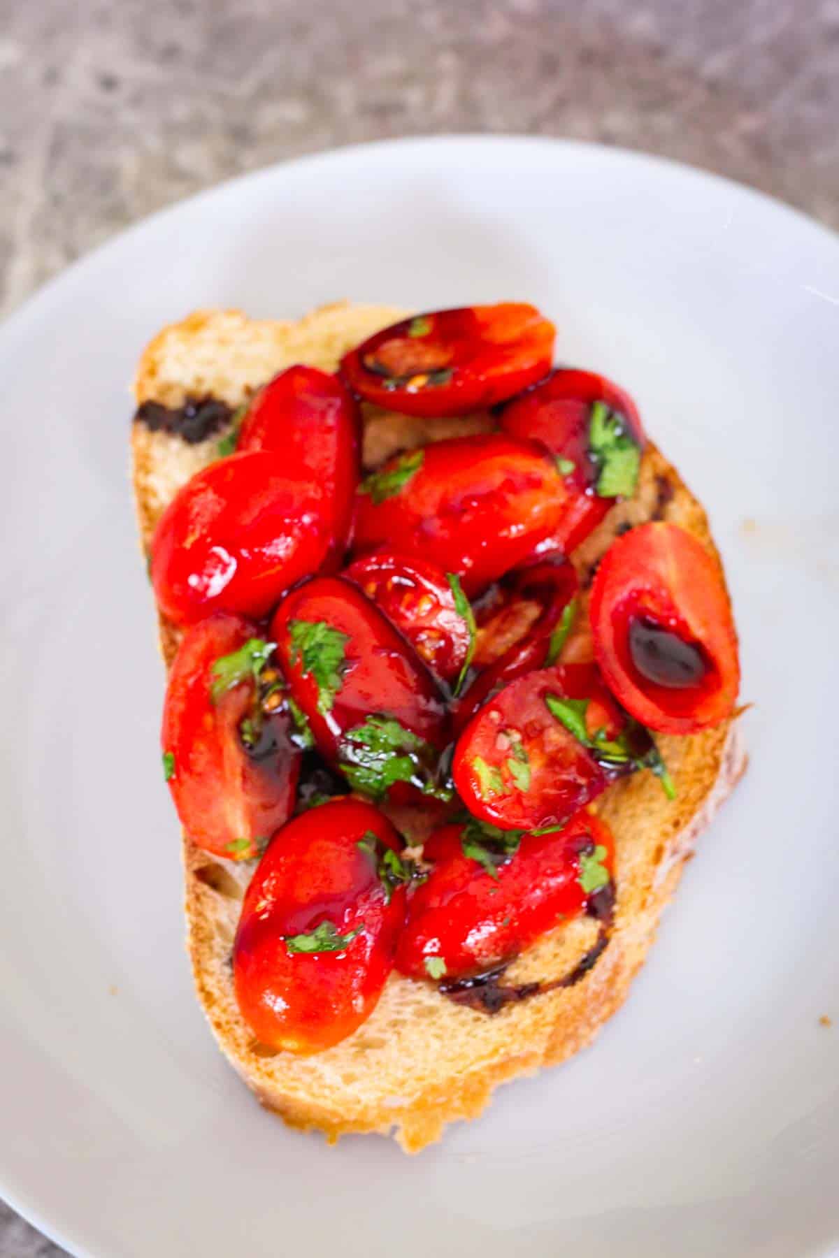 Toast on a plate topped with cherry tomatoes and drizzled with balsamic glaze.