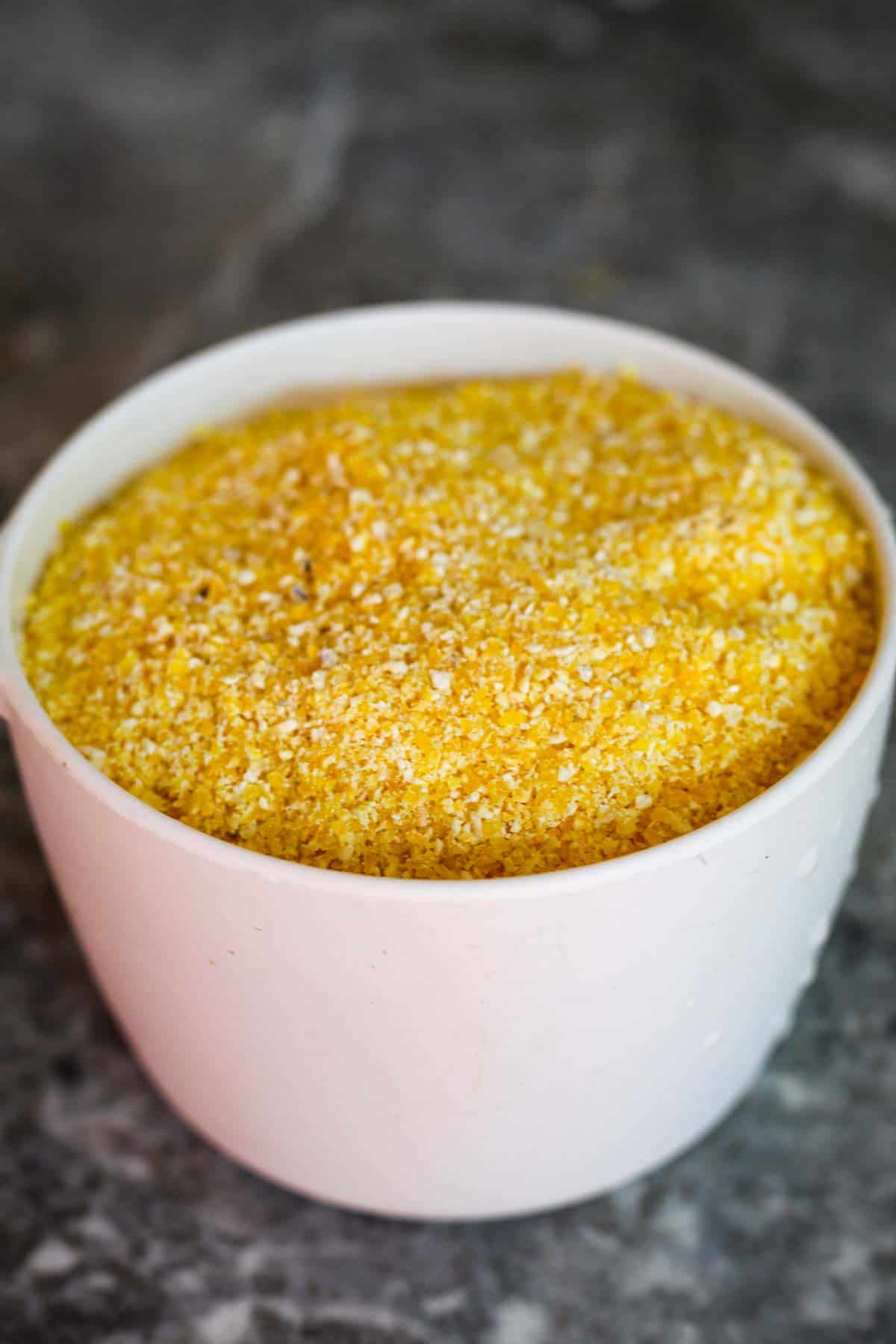 A cup of uncooked polenta, you can see the coarse yellow grains.