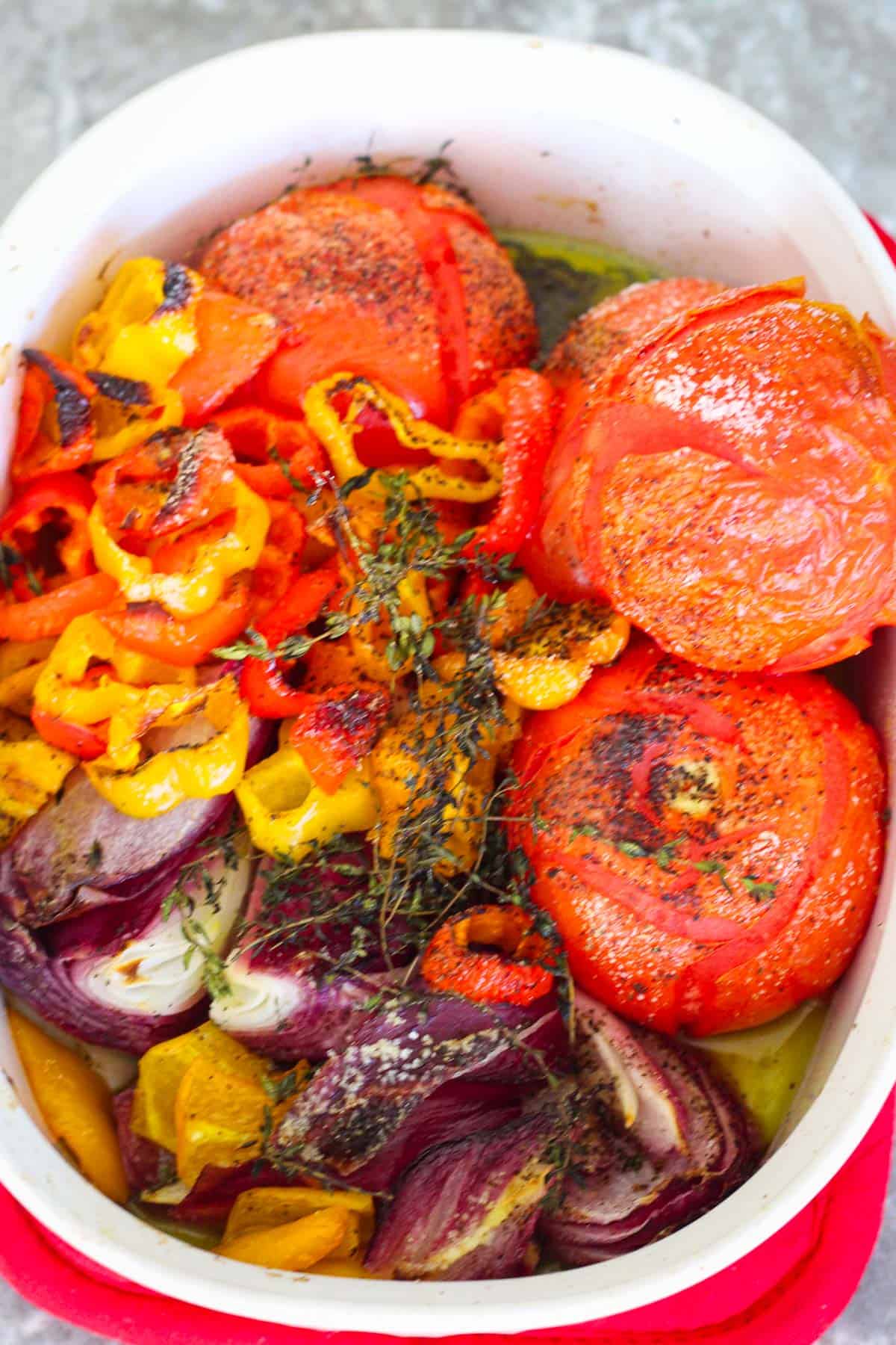 Tomatoes, peppers, onions and herbs on the baking tray after roasting.
