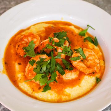 A white plate showing creamy polenta topped with shrimp, sauce and garnish.