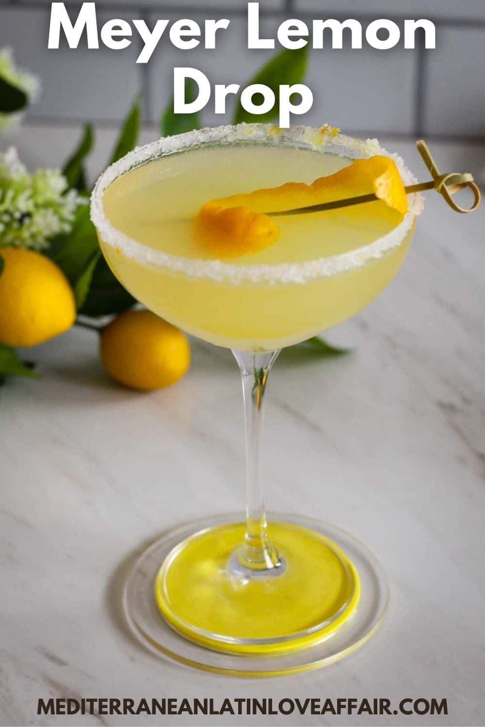 An image prepared for Pinterest. It shows a picture of a cocktail glass with Meyer Lemon Drop cocktail garnished with lemon peel. Picture has a title bar on top and website link at the bottom.