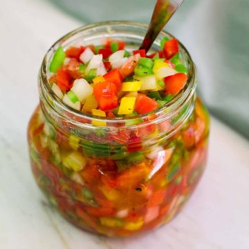 A glass jar filled to the top with salsa criolla and there's a spoon in the jar too.
