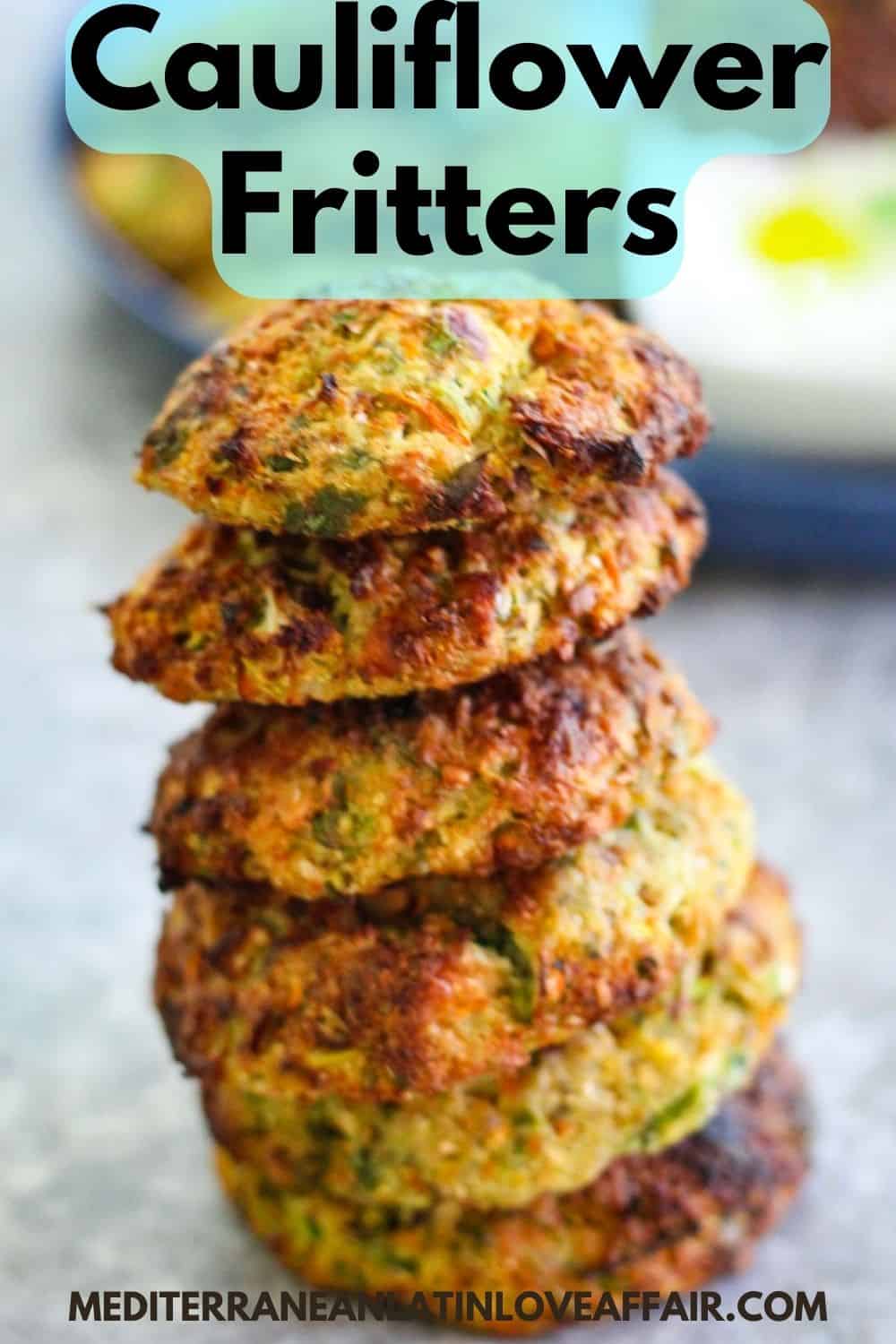 An image prepared for Pinterest. It shows a picture of stacked cauliflower fritters front and center with additional, blurred food items in the background. Picture has a title bar on top and the website link on the bottom. 
