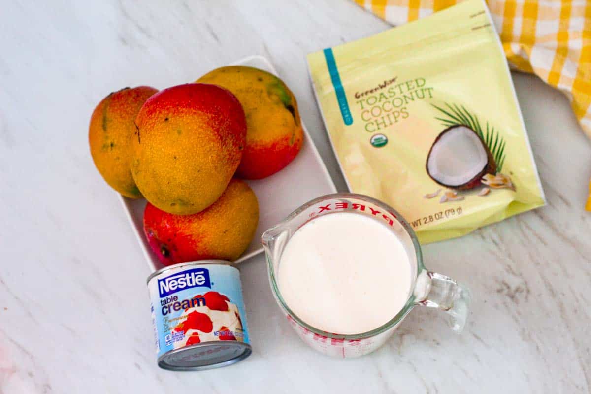 Ingredients for making mango mousse: fresh mangoes, table cream, heavy whipping cream, toasted coconut chips. 